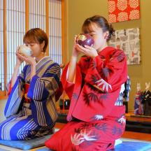 two young girls in kimonos sitting on the floor drinking from donuts