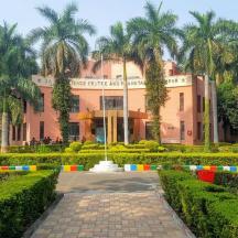 a pink building with palm trees in front of a garden
