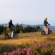 dues persones que van amb moto en un turó amb flors