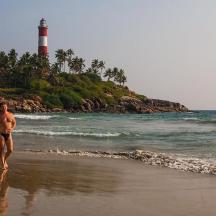 a man and woman walking on the beach with a lighthouse in the background