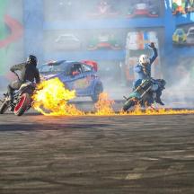 two people riding motorcycles on a track with fire