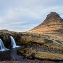 a waterfall in a field with a mountain in the background