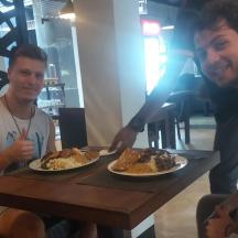 two men sitting at a table with plates of food