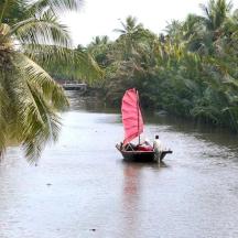 a boat with a red sail on a river with palm trees