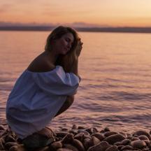 eine Frau in einem weißen Kleid sitzt an einem felsigen Strand