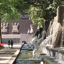 two people walking down a sidewalk next to a fountain