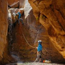 two people are rappelling from a rock formation