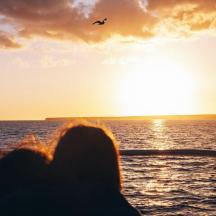eine Person, die auf einem Schiff sitzt und den Sonnenuntergang betrachtet