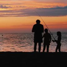 a man and two children fishing on the beach at sunset
