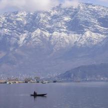 eine Person in einem Boot im Wasser mit schneebedeckten Bergen