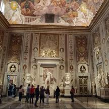 a group of people walking in a large room with paintings on the walls