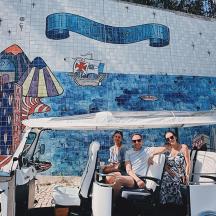 three people sitting in a golf cart in front of a mural