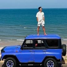 a man standing on top of a blue jeep on the beach