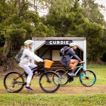 two people riding bikes in front of a kiosk