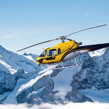 a yellow helicopter flying over a snowy mountain