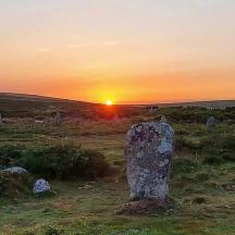 un tramonto su un campo con una grande roccia