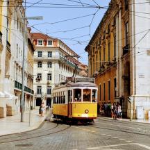 a yellow tram on a city street with buildings