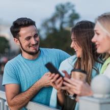 ein Mann und zwei Frauen schauen auf ein Mobiltelefon
