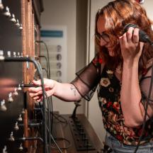 a woman talking on a microphone next to a wine rack