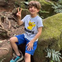 a young boy sitting on a rock giving the peace sign