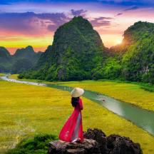 a woman in a red dress standing on a rock overlooking a river