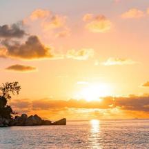 a sunset over the ocean with a rocky island