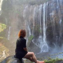 a woman sitting on a rock in front of a waterfall