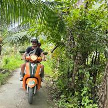 two people riding on an orange scooter on a dirt road