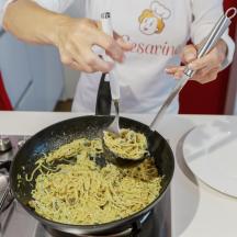 una persona che cucina i noodles in una padella su un fornello