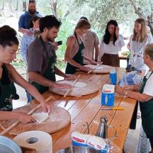 a group of people standing around a table making pizzas