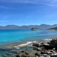 a beach with blue water and rocks and mountains