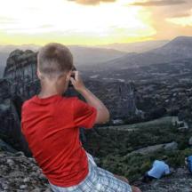 a boy talking on a cell phone on top of a mountain