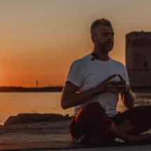 un home assegut a la platja mirant la posta de sol