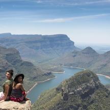 two people sitting on top of a mountain overlooking a river