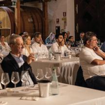 un grup de persones assegudes a taules amb copes de vi