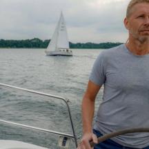 a man standing on the front of a boat with a sailboat