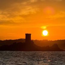 ein Sonnenuntergang über dem Meer mit einem Leuchtturm in der Ferne