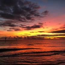 a sunset on the beach with a person in the water
