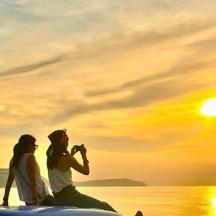 a man and a woman sitting on the beach at sunset
