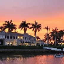 a large house with palm trees and a boat in the water