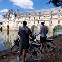 two men standing with their bikes in front of a castle