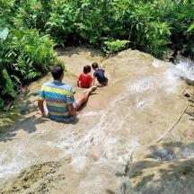 three people sitting on a rock near a river