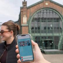 Eine Frau hält vor einem Gebäude ein Handy hoch.