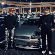 two men standing next to a car in a parking lot