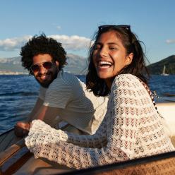 Two people lean on the edge of a boat and smile in the sunshine. 