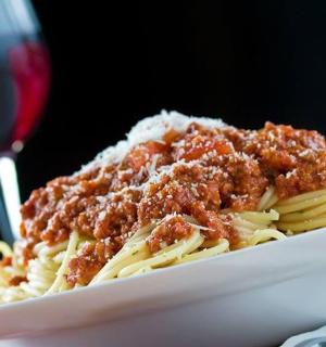 a plate of pasta with meat sauce and a glass of wine