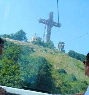 two people on a gondola looking at a cross on a hill
