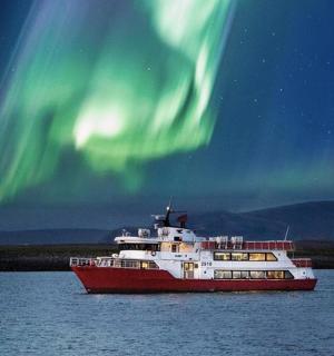 a red and white boat in the water under the northern lights