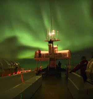 an image of a ship with the green northern lights