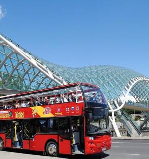 a red double decker bus driving under a bridge